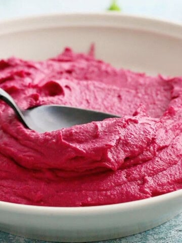 pink beet hummus in a white bowl with a black spoon.