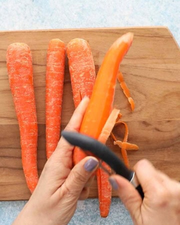 two hands peeling the skin from a carrot.