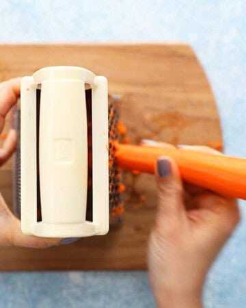 two hands grating one carrot using a box grater.
