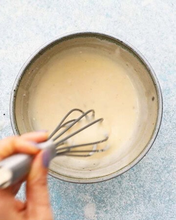 a hand whisking white dressing in a blue bowl.