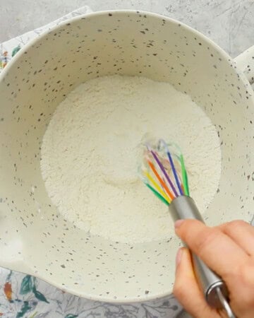 a hand whisking flour in a white bowl.