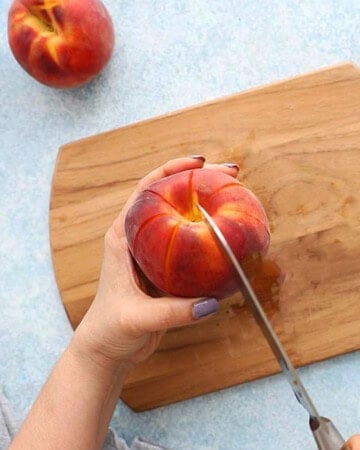 two hands cutting one peach into wedges.