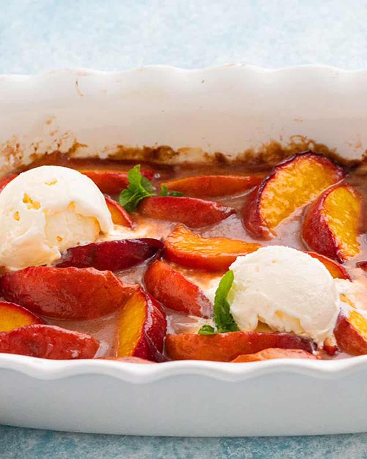 baked peaches topped with two scoops of white ice cream in a white dish.