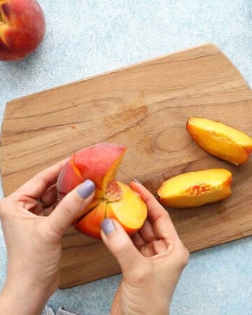 two hands cutting one peach into wedges.