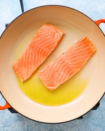 two salmon fillets cooking in a large white skillet.