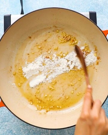 a hand cooking flour and minced garlic in a large white skillet. 