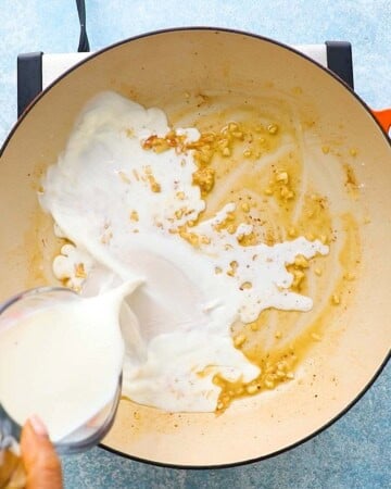 a hand pouring white milk into a large white skillet.