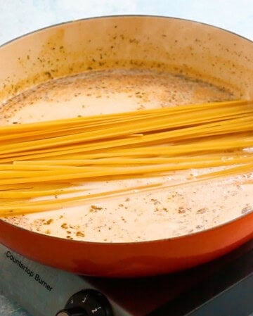 raw fettuccini in a white sauce in a large skillet.