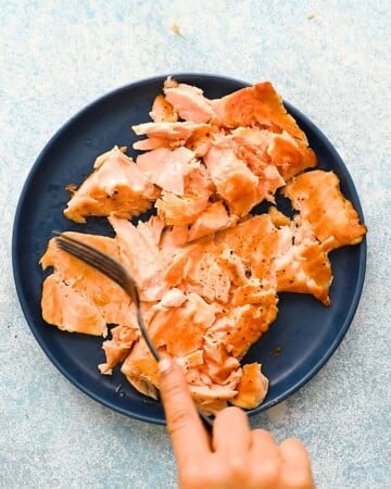 a hand breaking cooked salmon fillets into chunks.