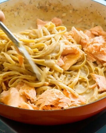 a hands tossing cooked salmon pasta using tongs.