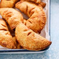 apple hand pies placed on a parchment lined white metal tray.