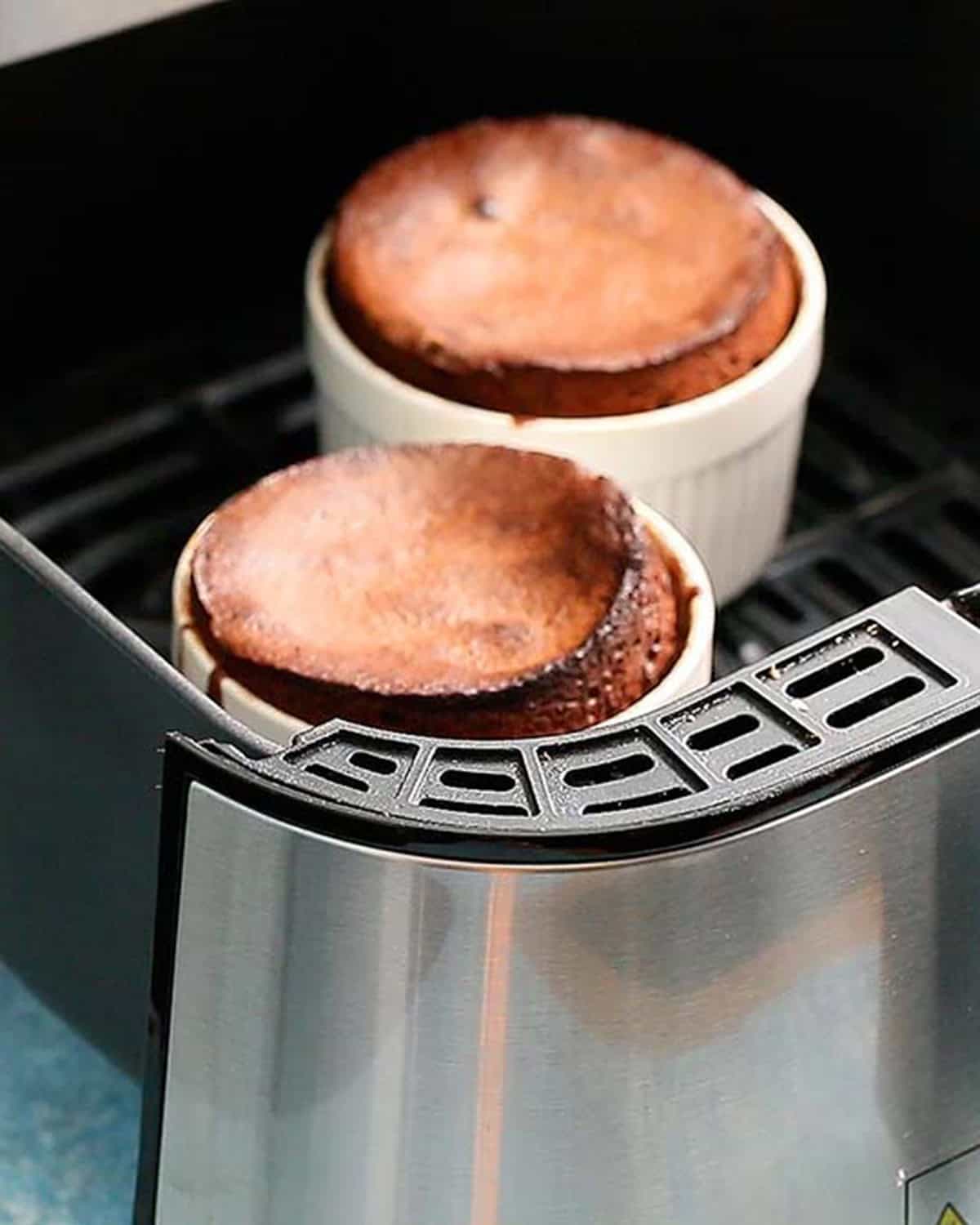 two cooked chocolate lava cakes in an air fryer basket.