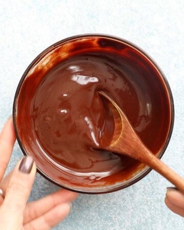 two hands mixing brown melted chocolate in a glass bowl.