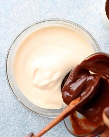 two hands pouring brown chocolate mixture into a glass bowl.