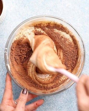 two hands mixing chocolate lava cake batter in a glass bowl.