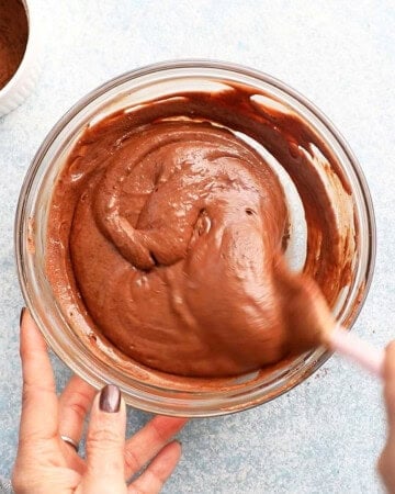 two hands mixing chocolate lava cake batter in a glass bowl.