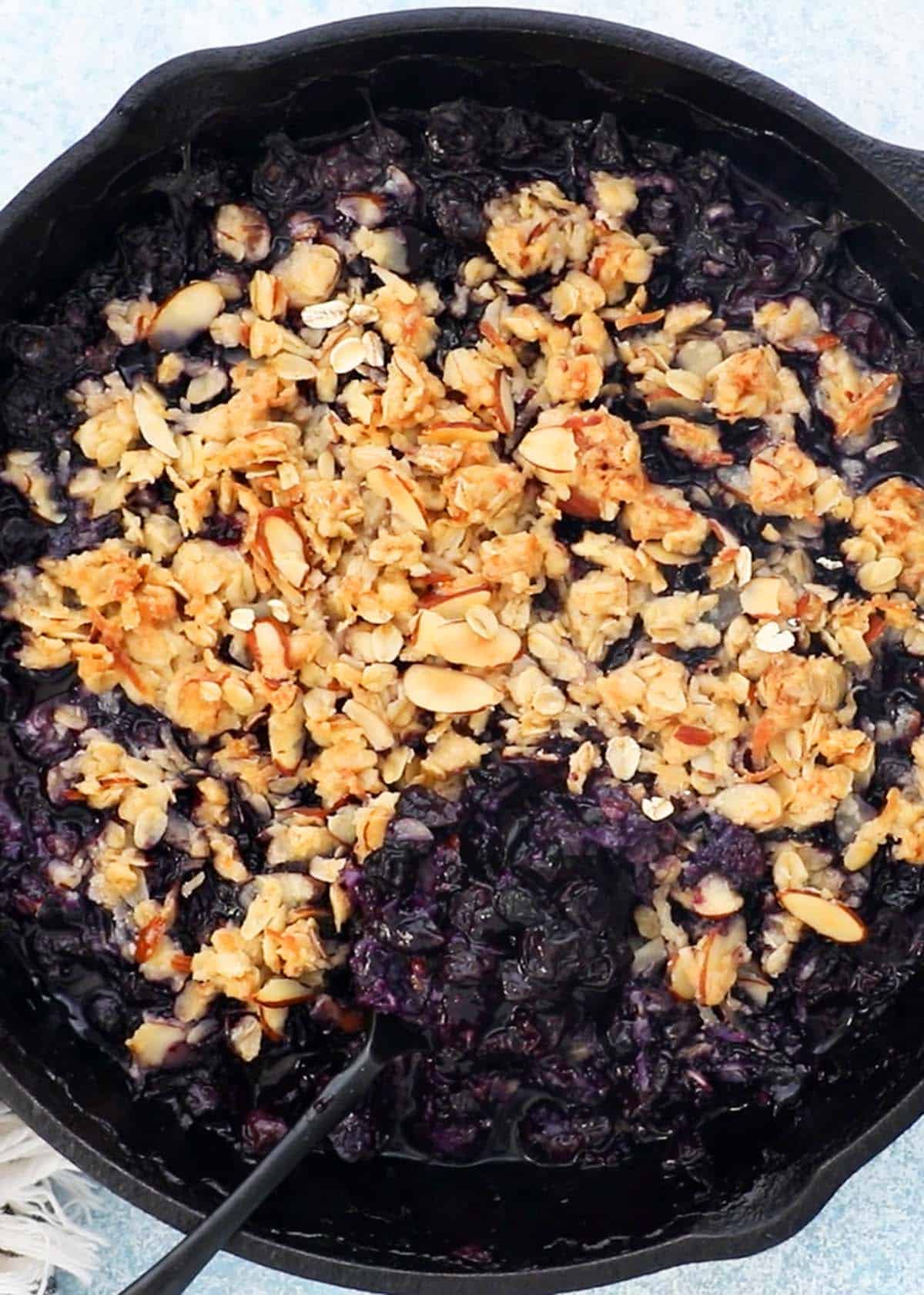 baked blueberry crisp with crumble topping in a black skillet.