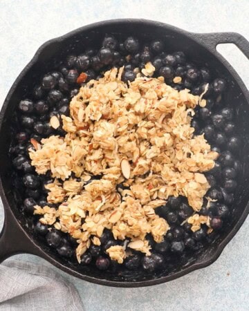 crumble topping over blueberries in a black skillet.