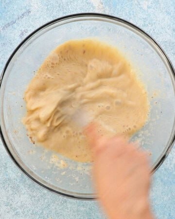 two hands whisking wet batter in a large glass bowl. 