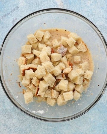 cubed bread placed on top of wet batter in a large glass bowl.