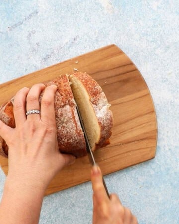 two hands slicing one loaf of bread into slices.