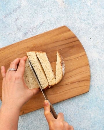two hands cutting one slice of bread into square pieces.