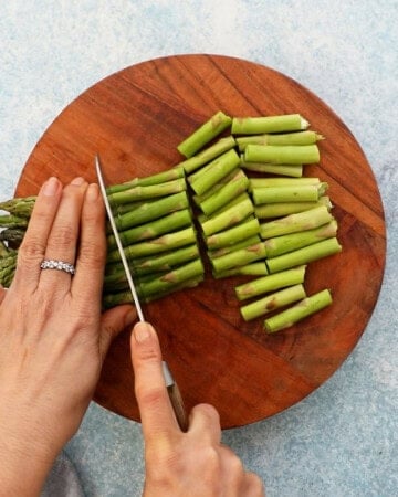 two hand cutting a bunch of asparagus into chunks.