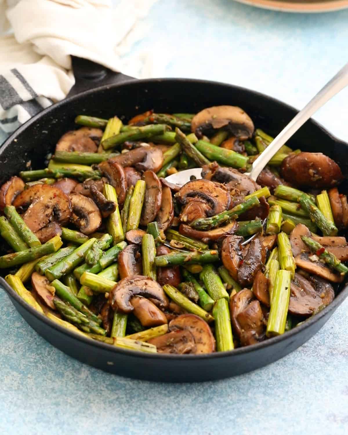 one black skillet filled with sauteed mushrooms and asparagus.