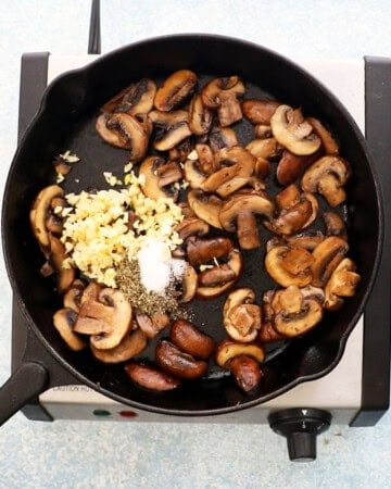 sauteed mushrooms along with freshly chopped garlic in a black skillet.