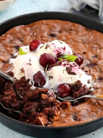 chocolate brownies topped with white ice cream in a black skillet.