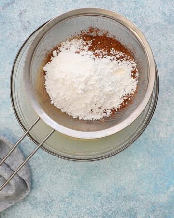 one strainer with white flour and brown cocoa placed over a large glass bowl.