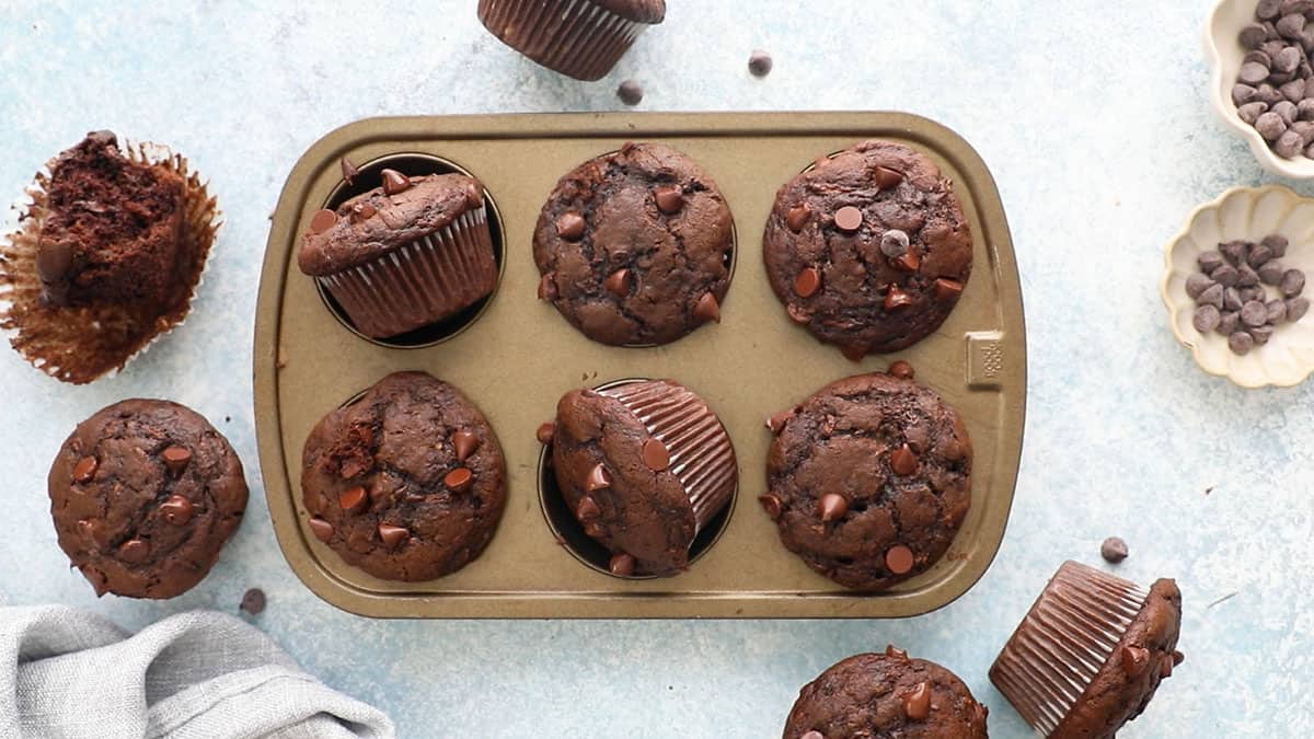 6 baked chocolate zucchini muffins placed in a metal muffin pan.