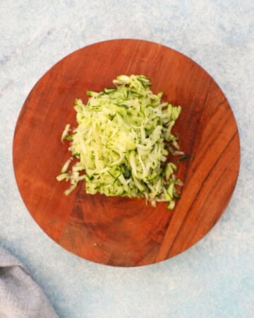 pile of grated zucchini on a round wooden cutting board.