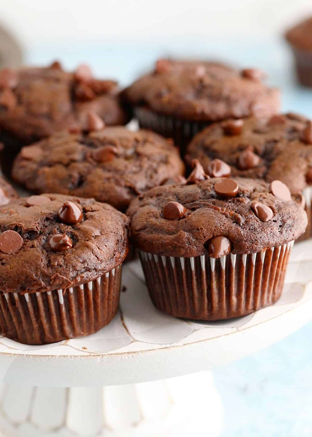 6 chocolate zucchini muffins placed on a white cake stand.