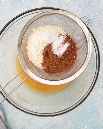 white flour and brown cocoa powder placed on a sieve placed on a large glass bowl.