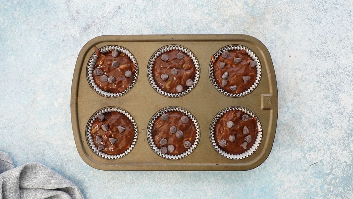 a 6 cup muffin tray filled with brown chocolate muffin batter.