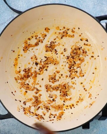 a hand cooking minced onion and garlic in a large white skillet.