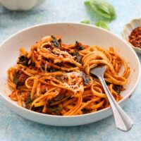 cooked fettuccini pasta tossed in red sauce placed in a white bowl.