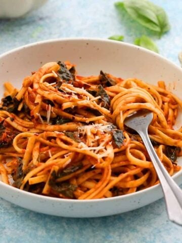 cooked fettuccini pasta tossed in red sauce placed in a white bowl.