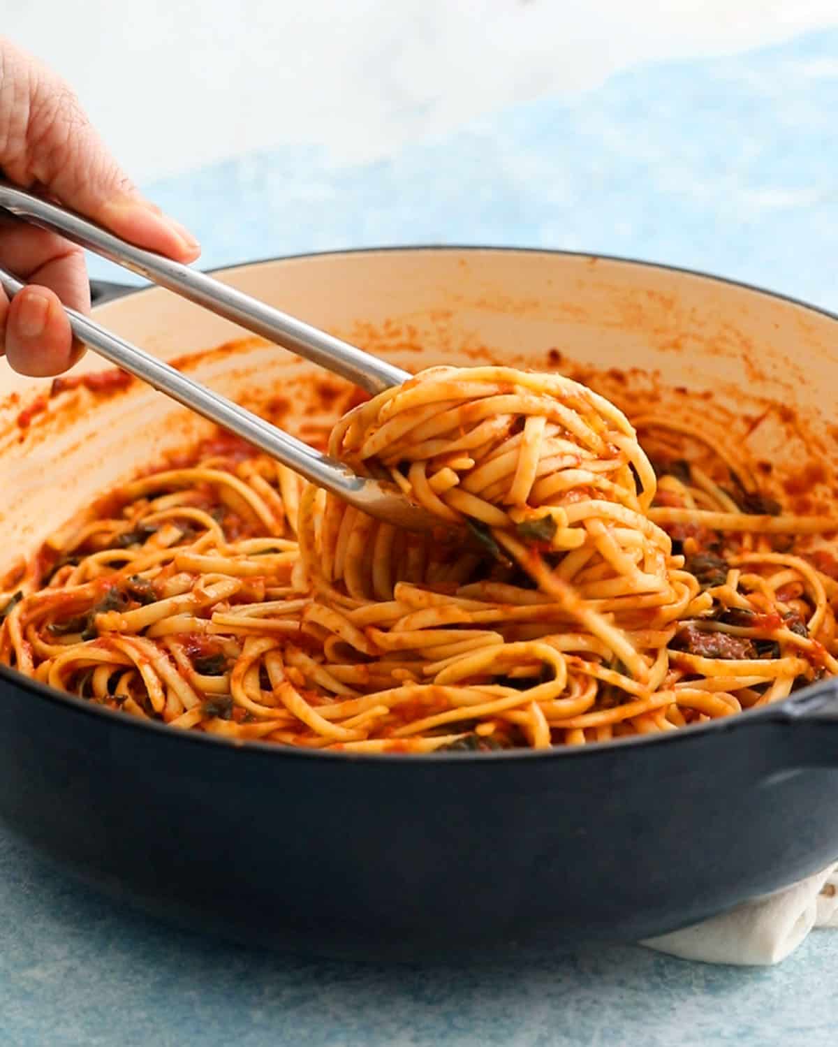 a hand removing cooked red sauce pasta using a metal tongs. 