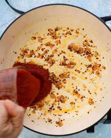 a hand pouring red tomato sauce into a large white pan.