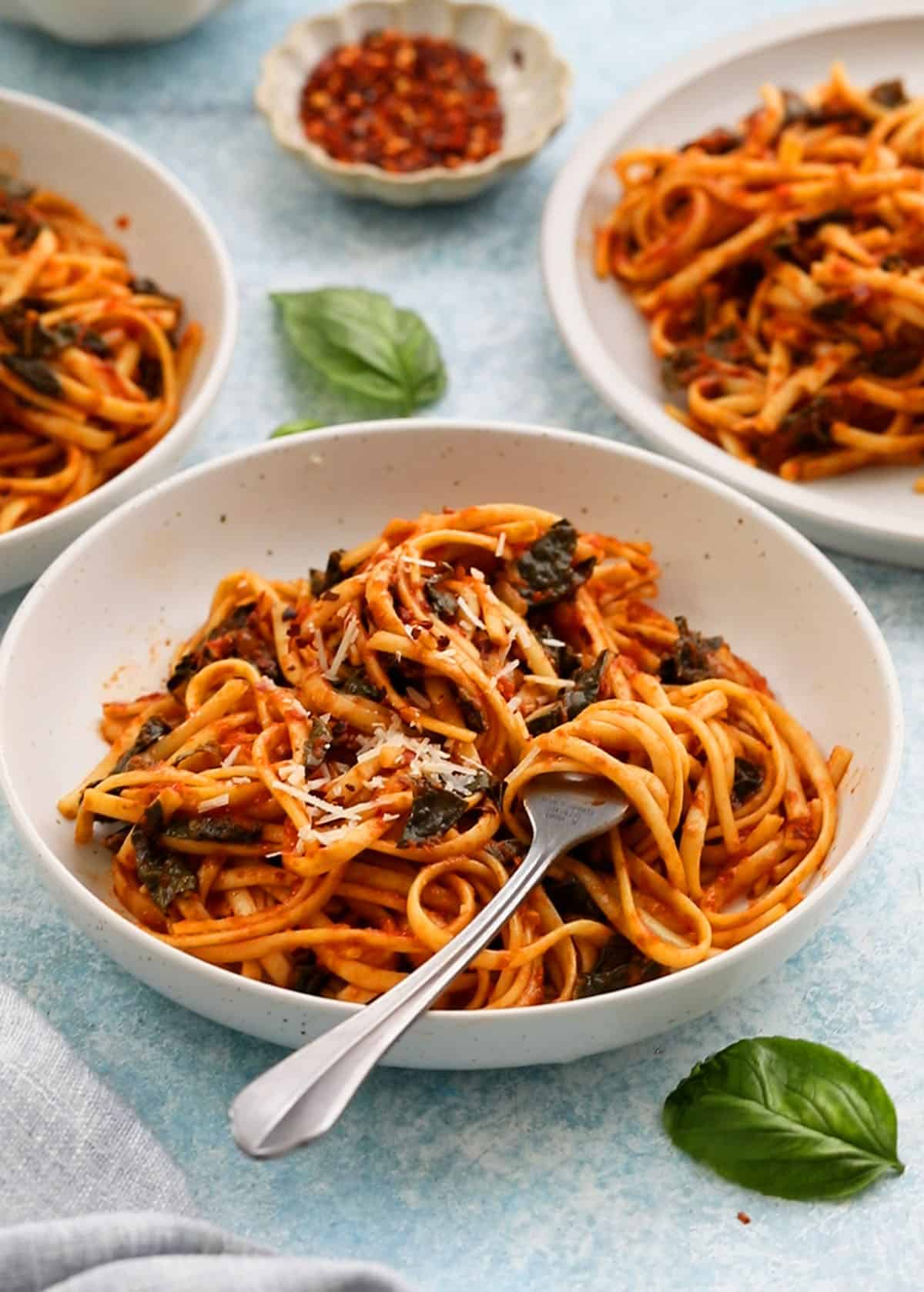 three white plates with cooked red sauce pasta along with forks.