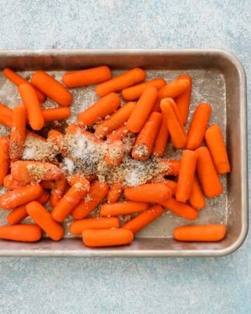 raw baby carrots topped with seasoning in a metal sheet pan. 