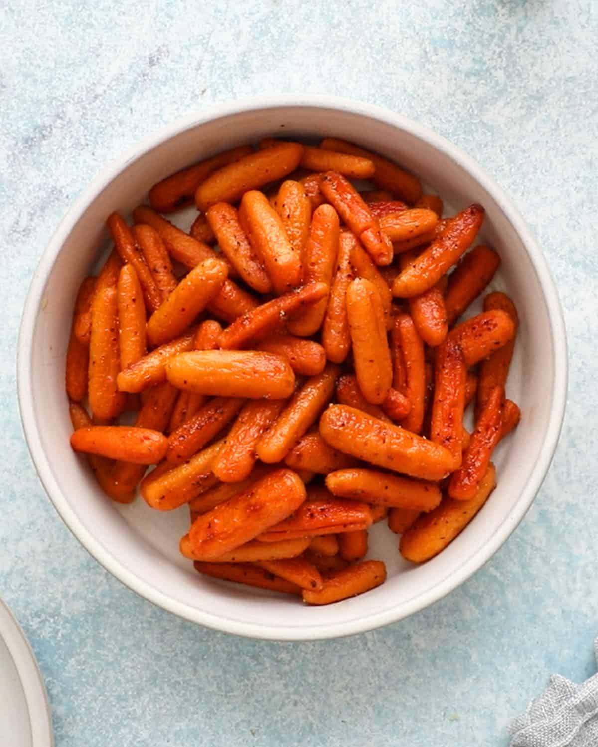 roasted orange baby carrots in a round white bowl.