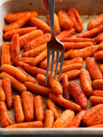 roasted baby carrots in a metal sheet pan along with a fork.