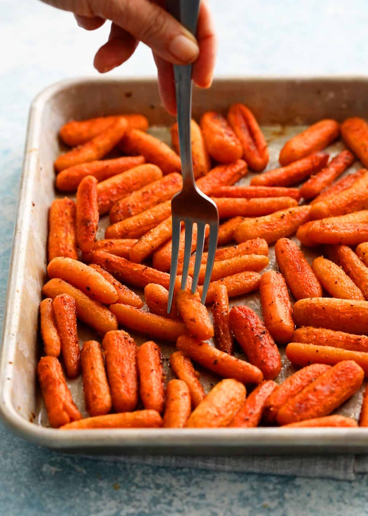 roasted baby carrots in a metal sheet pan along with a fork.