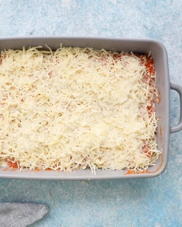 white shredded cheese on top of pink sauce in a grey baking dish.