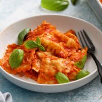 cooked ravioli in red sauce in a round white plate along with a black fork.