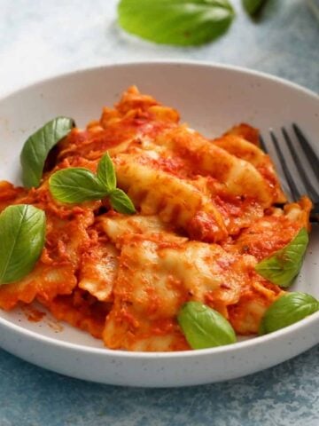 cooked ravioli in red sauce in a round white plate along with a black fork.