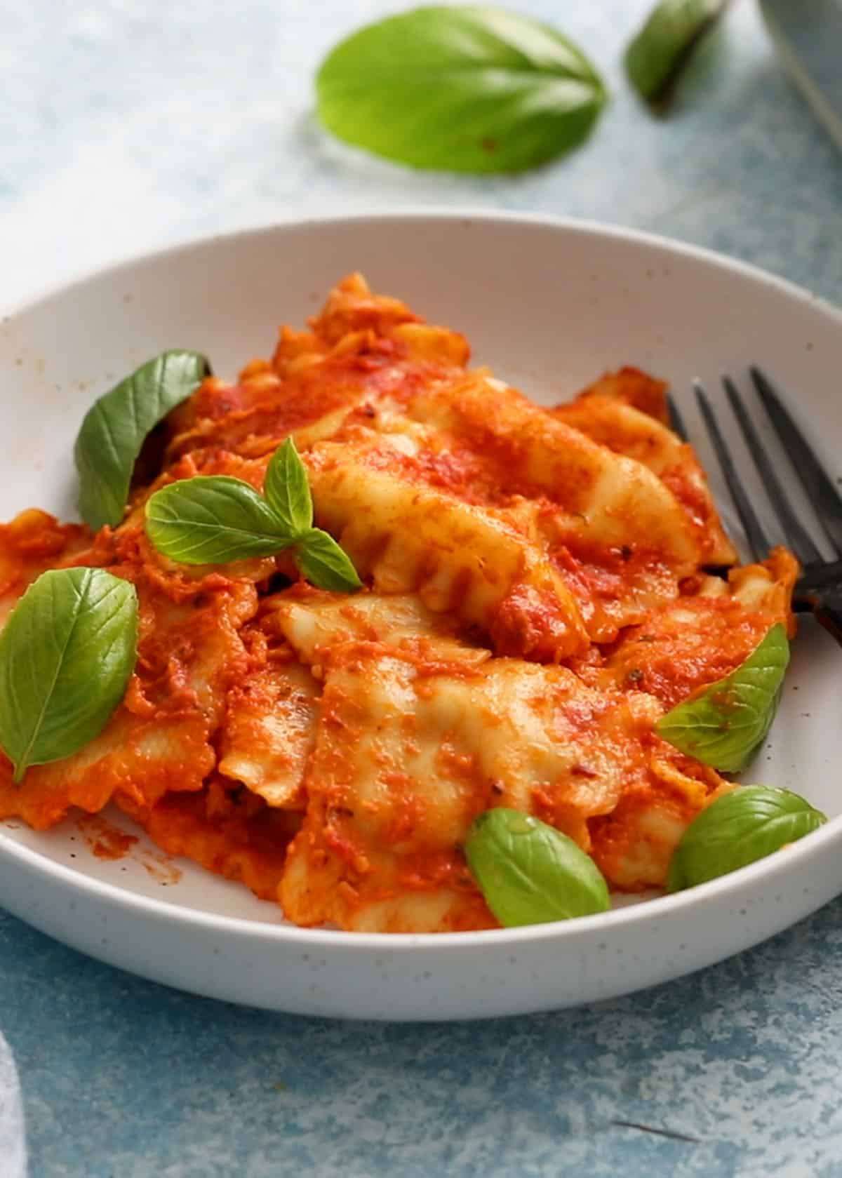 cooked ravioli in red sauce placed in a white plate along with a black fork.